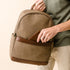 Brown waxed canvas NISOLO backpack with leather trim being held by a person placing a wallet in the front pocket.