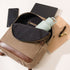 Open tan canvas NISOLO backpack with a light green water bottle, laptop, notebook, and keys on a white surface.