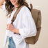 Olive green waxed canvas backpack with brown leather trim worn by a person in a white shirt.