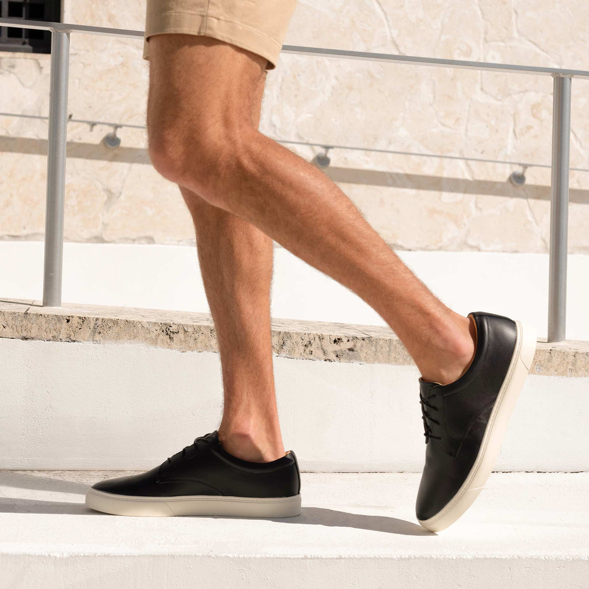 Pair of black leather Diego Everyday Sneakers with white soles worn by a person walking on white stone steps.