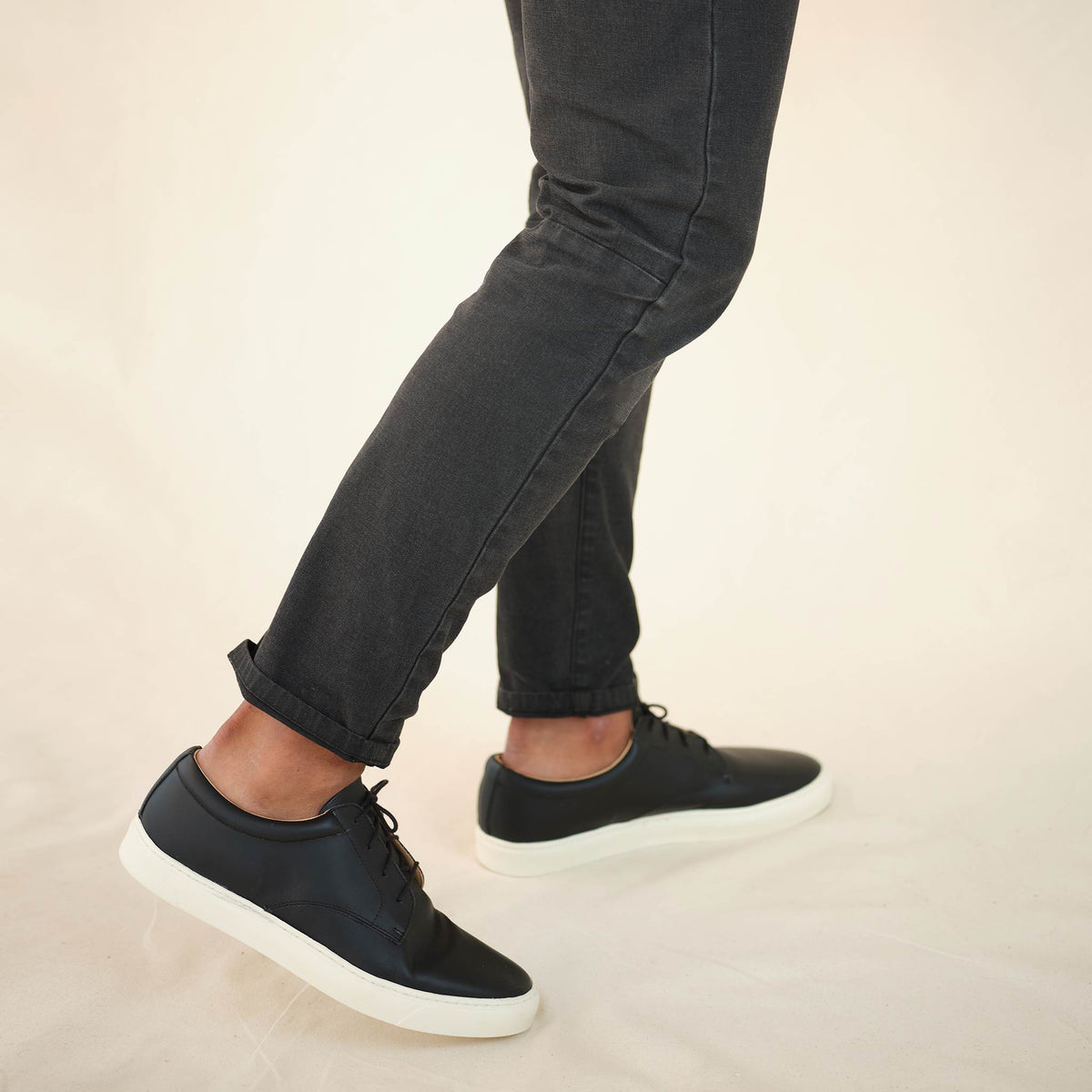 Pair of black leather Diego Everyday Sneakers with white soles worn with dark grey pants.