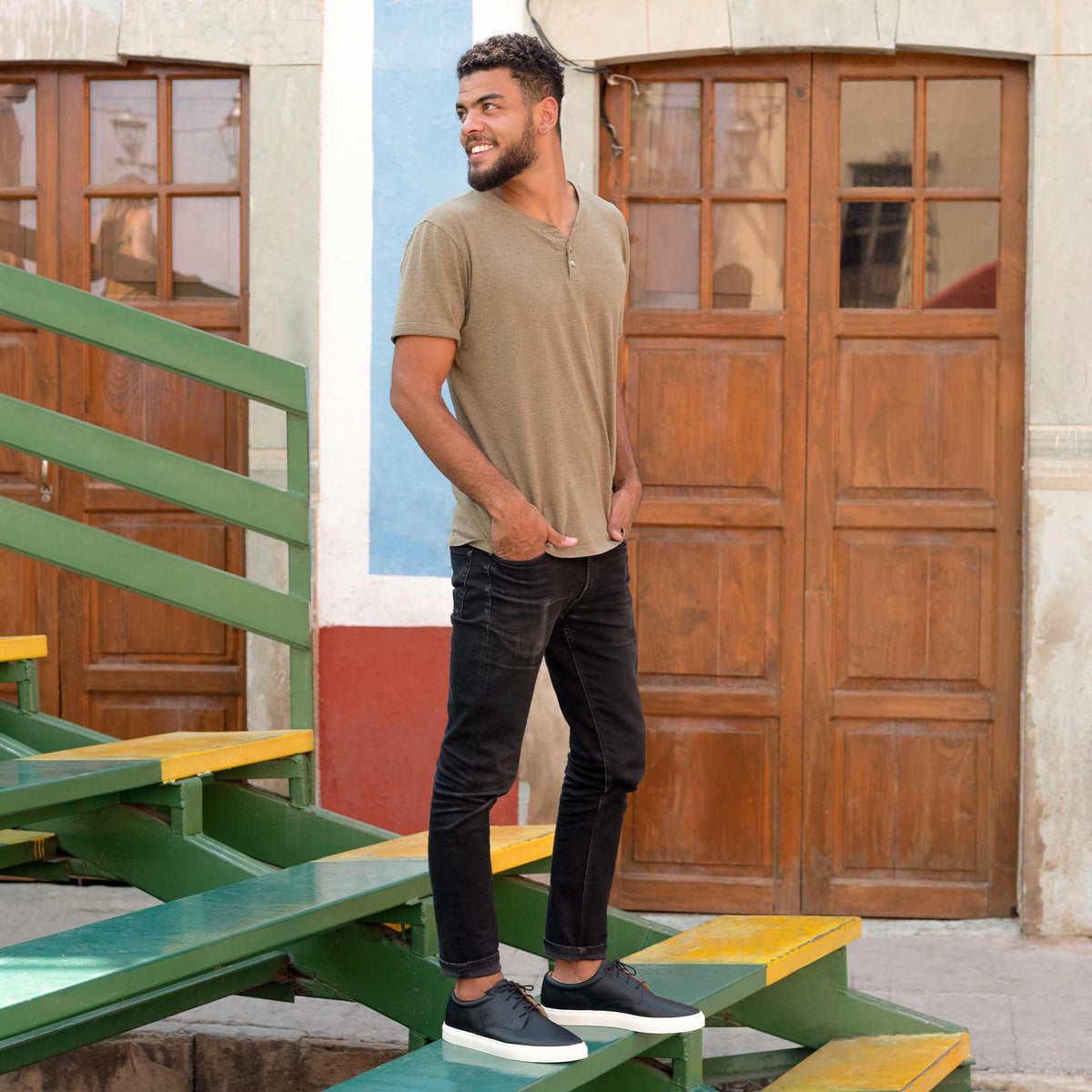 Man standing on green and yellow stairs wearing black leather Diego Everyday Sneakers with white soles.