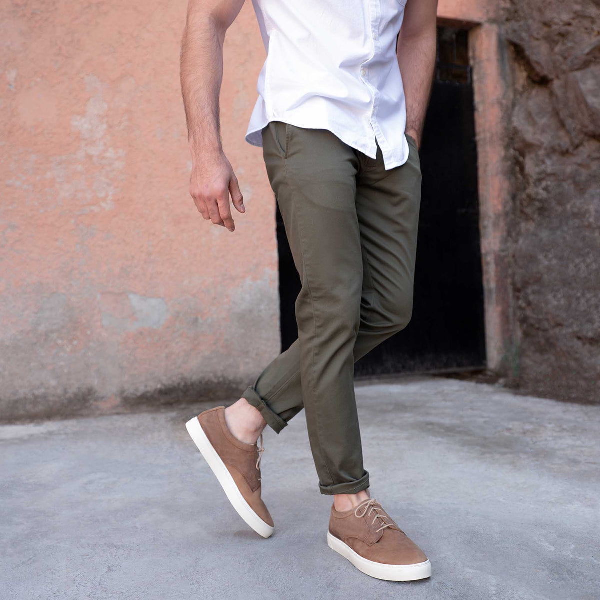 Pair of tobacco brown leather sneakers with white soles worn with olive pants and a white shirt.