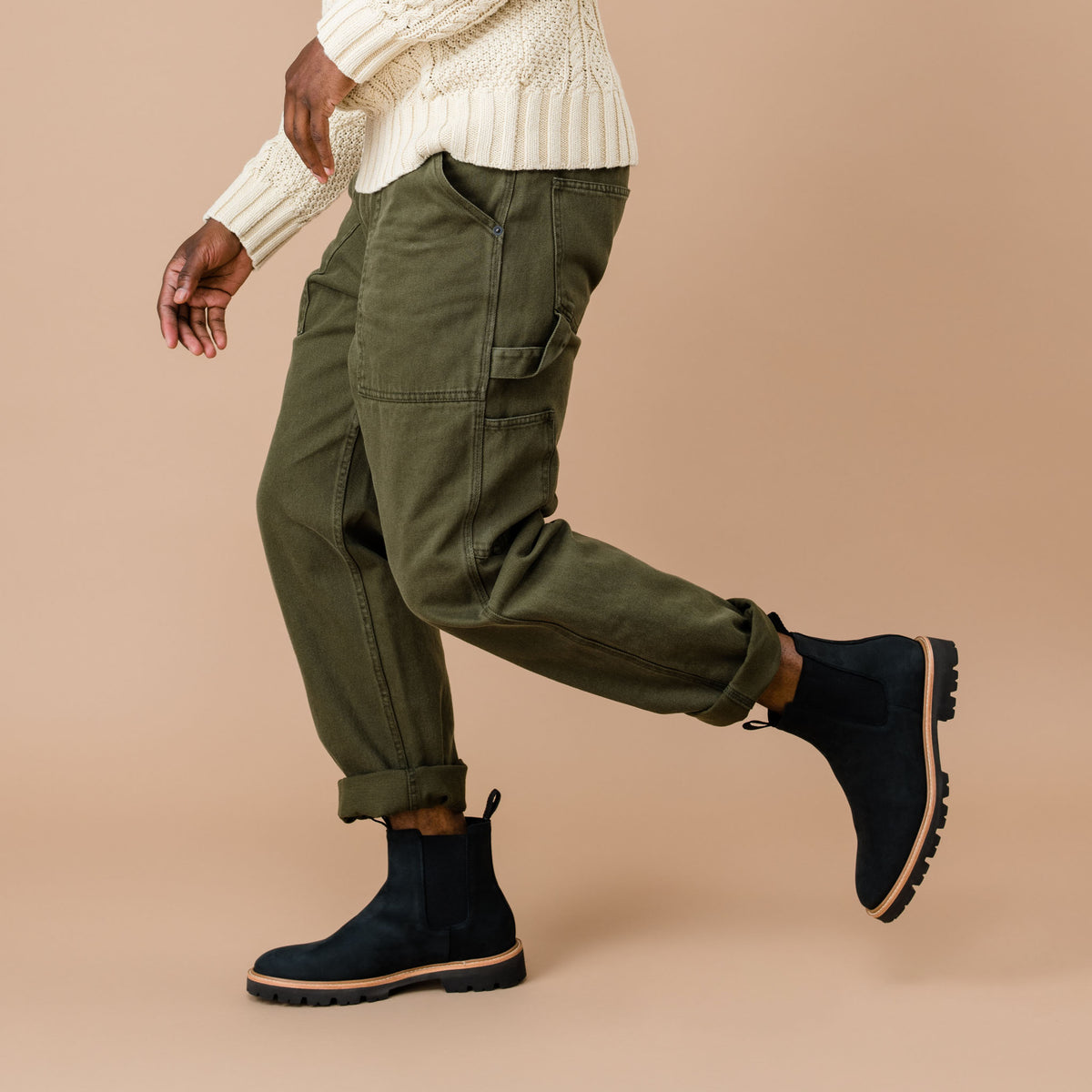 Pair of black leather Chelsea boots with lug soles worn with olive green pants and a cream sweater.
