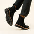 Pair of black fabric Chelsea boots with lugged rubber soles worn by a person in dark trousers.