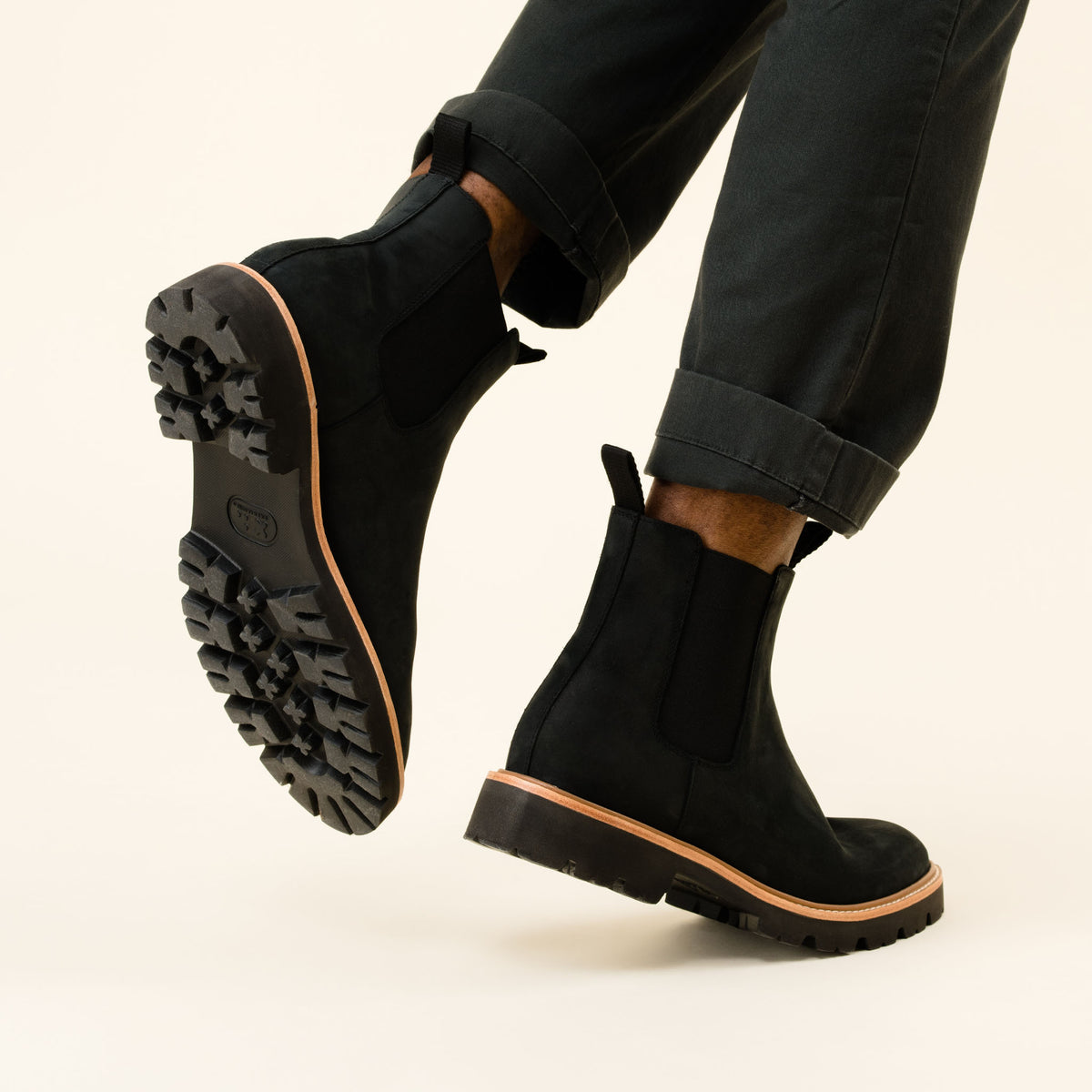 Pair of black fabric Chelsea boots with lugged rubber soles worn by a person in dark trousers.