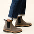 Pair of grey leather Chelsea boots with black elastic side panels and lug soles, worn with cuffed blue jeans.