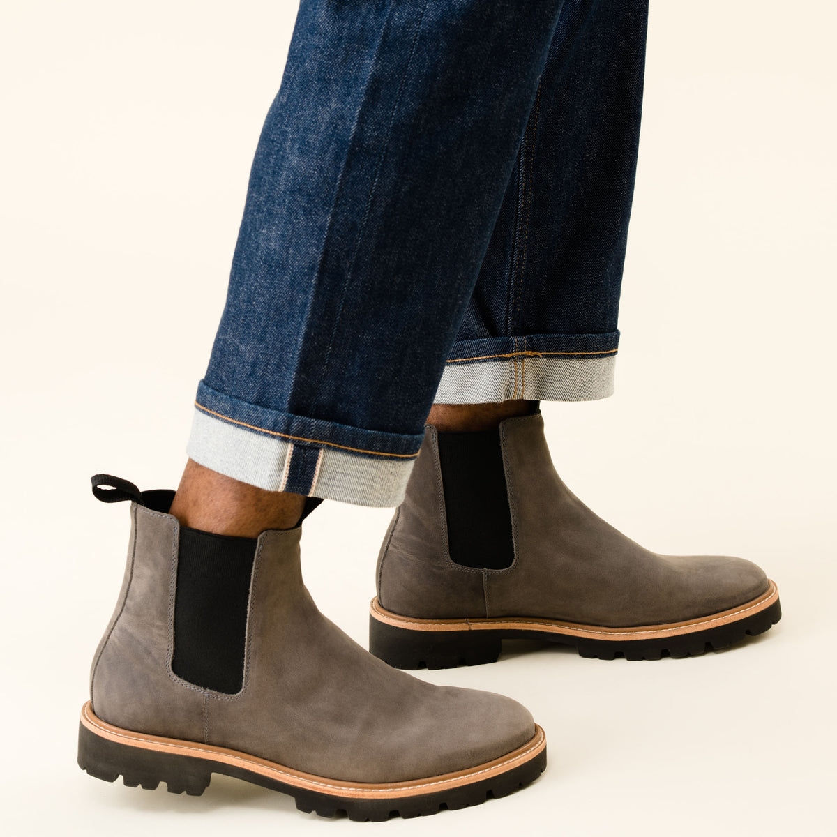 Pair of grey leather Chelsea boots with black elastic side panels and lug soles, worn with cuffed blue jeans.