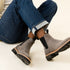 Two grey suede Chelsea boots with black elastic side panels and lug soles, worn with cuffed blue jeans.