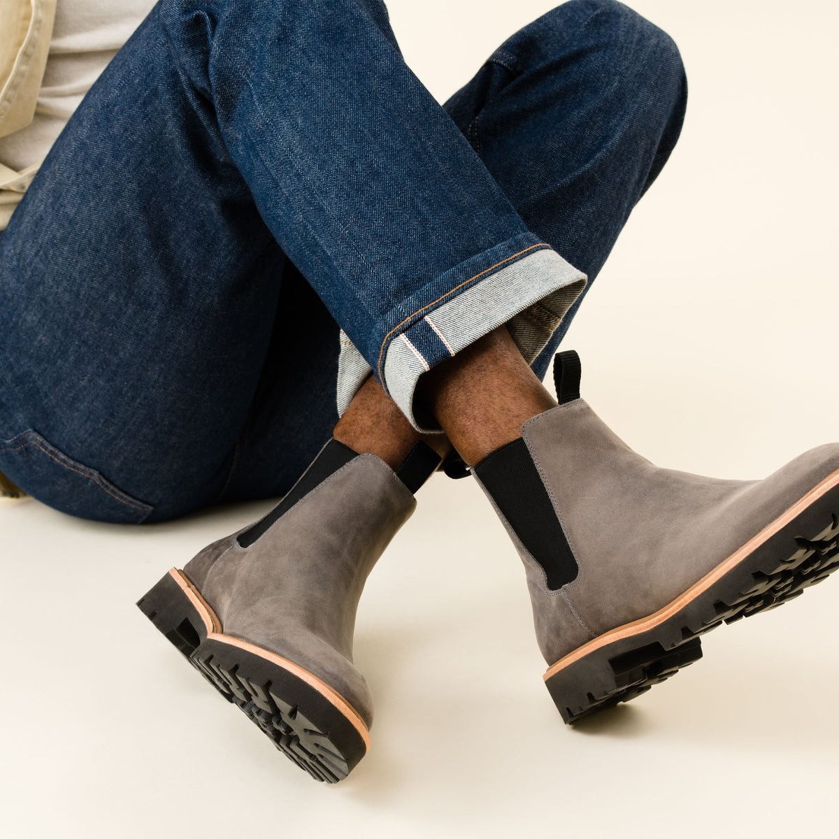 Two grey suede Chelsea boots with black elastic side panels and lug soles, worn with cuffed blue jeans.