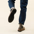 Grey leather Chelsea boots with black lug soles worn with blue denim jeans, showing the tread on one lifted foot.