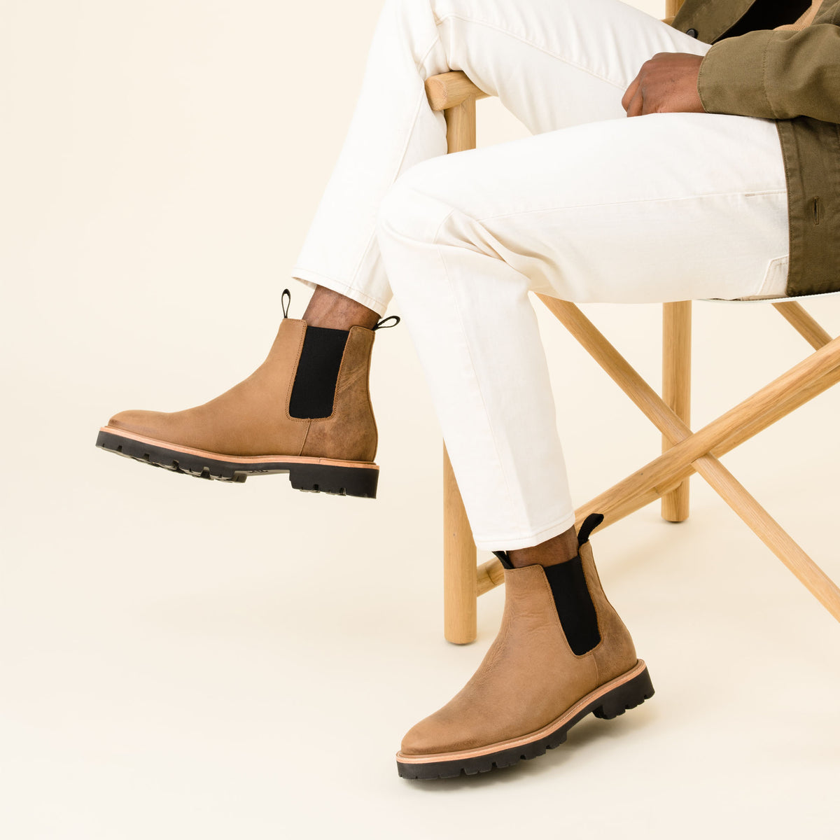 A pair of tobacco brown leather Chelsea boots with black elastic side panels and lug soles worn with white pants.