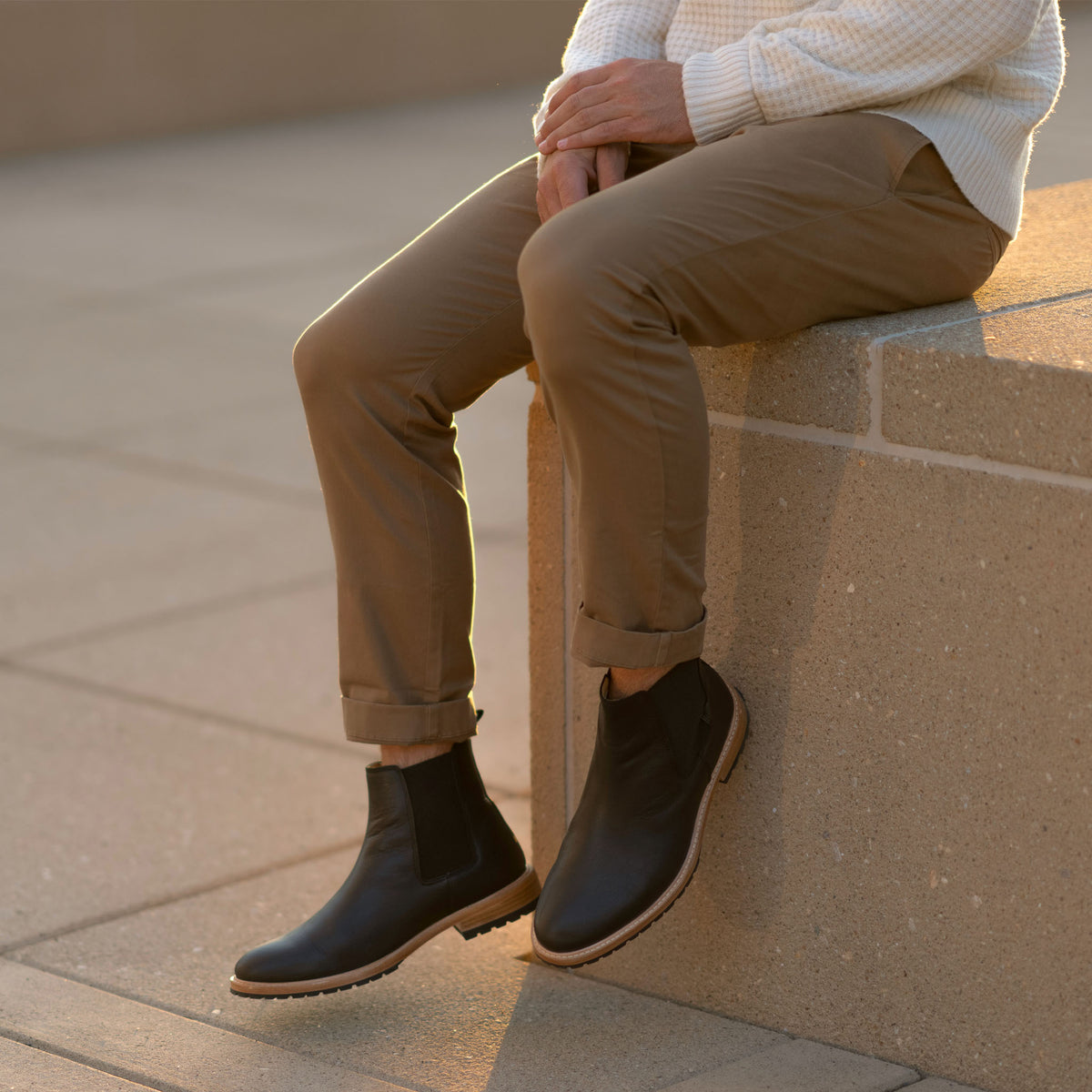 Pair of black leather Marco Everyday Chelsea boots worn by a person sitting on a stone ledge.
