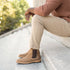 A person wearing tobacco brown leather Chelsea boots with dark elastic side panels, sitting on stone outdoor steps.