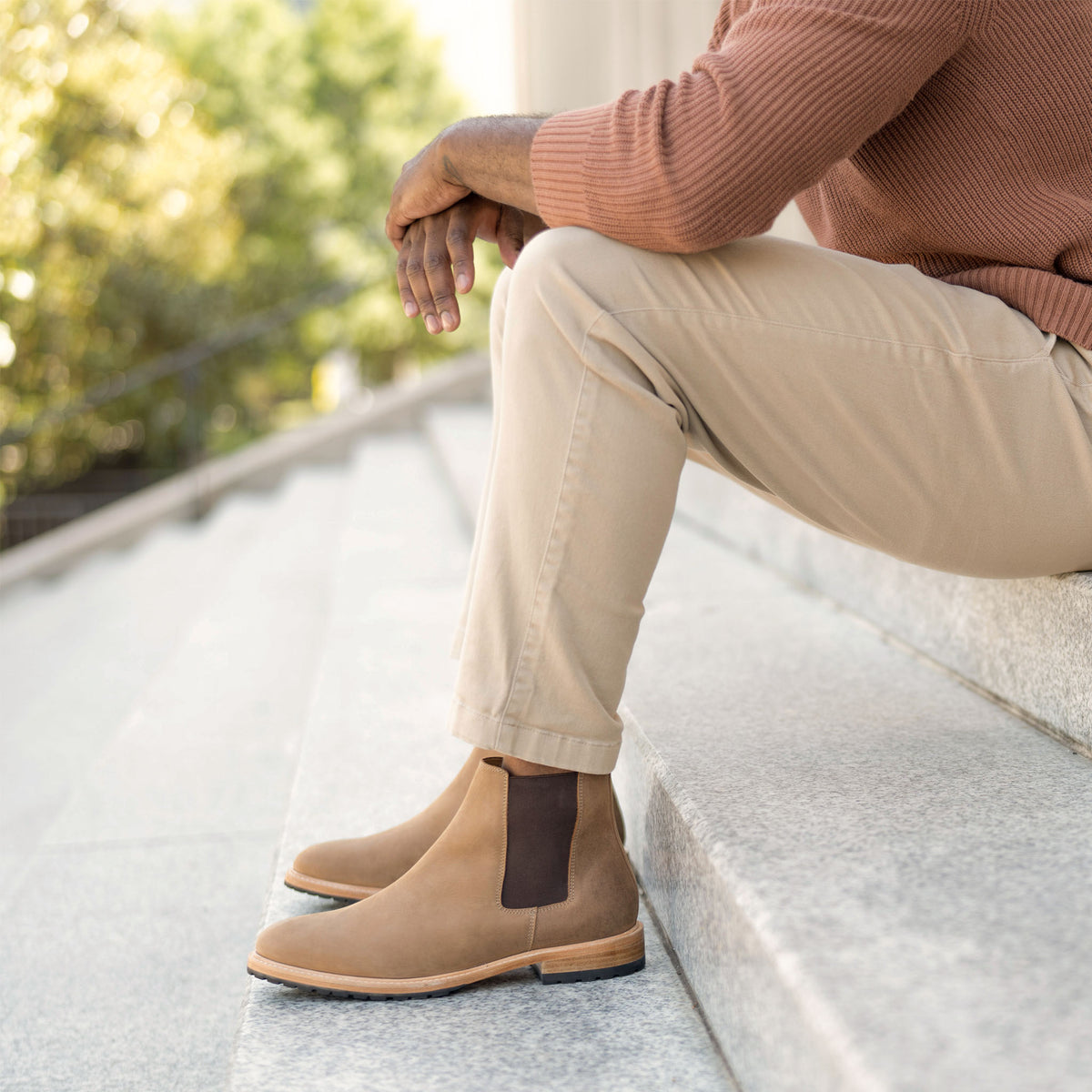 A person wearing tobacco brown leather Chelsea boots with dark elastic side panels, sitting on stone outdoor steps.