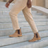 Two tobacco brown leather Chelsea boots with dark brown elastic side panels worn by a person walking up stone stairs.