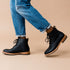 Pair of black leather Martin All-Weather Boots with tan soles worn with blue jeans on a tan background.
