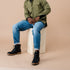 Pair of black leather lace-up boots worn with blue jeans by a person sitting on a wooden crate.