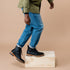 Pair of black leather Martin All-Weather Boots worn with blue jeans, stepping onto a light wood box.