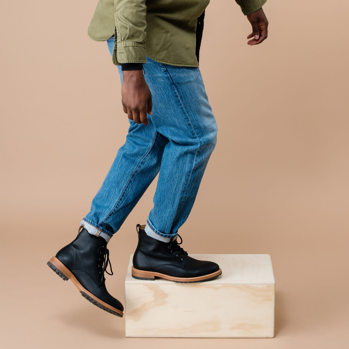 Pair of black leather Martin All-Weather Boots worn with blue jeans, stepping onto a light wood box.
