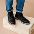 Pair of black leather lace-up boots worn with blue jeans, standing on a light wood box.
