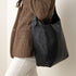 Black leather Cecilia Go-To Shoulder Bag worn over the shoulder of a person in a brown patterned blazer.