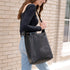 A person wearing a black leather Cecilia Go-To Shoulder Bag while walking past a light brick wall.