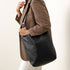 Black leather Cecilia Go-To Shoulder Bag with an adjustable strap worn over the shoulder of a person in a plaid blazer.