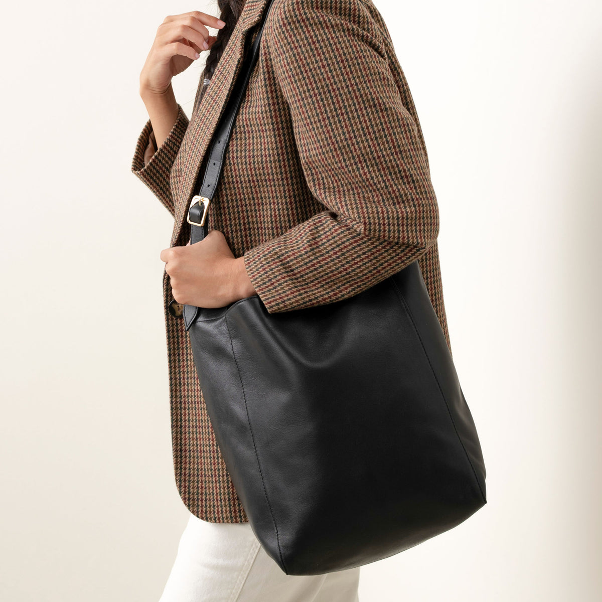 Black leather Cecilia Go-To Shoulder Bag with an adjustable strap worn over the shoulder of a person in a plaid blazer.