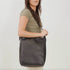 One black rectangular leather shoulder bag with a thin strap worn by a person in a green shirt.