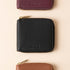 Three square leather wallets in black, plum, and brown with gold zippers and the NISOLO logo embossed on the front.