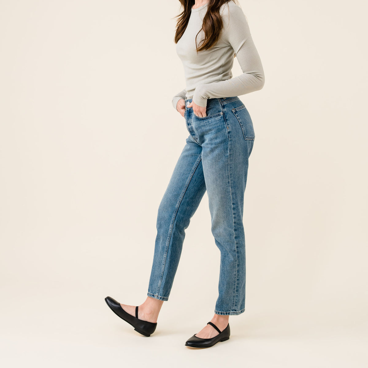 Pair of black leather Mary Jane flats worn by a person in blue jeans and a grey long-sleeve shirt.