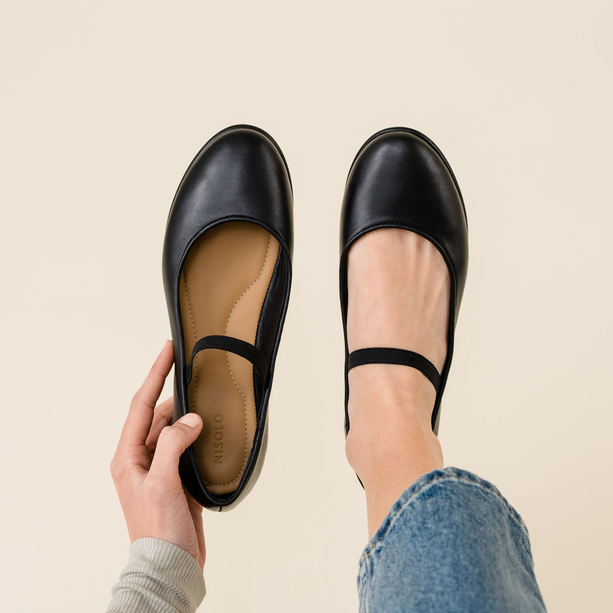 Pair of black leather Mary Jane flats with elastic straps and NISOLO printed on the tan insole.