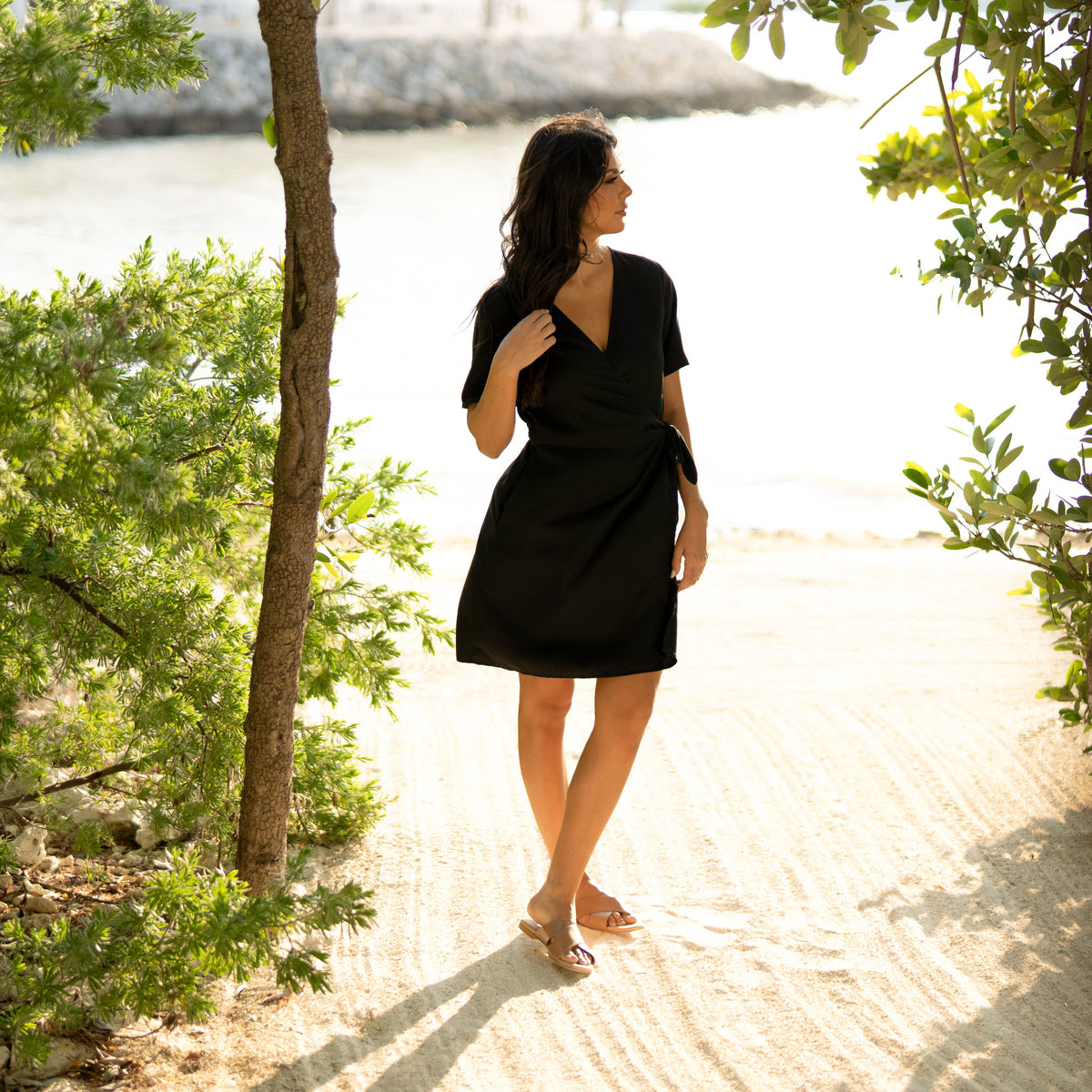 Woman in a black dress wearing almond leather Catalina Slide Sandals on a sandy path outdoors.