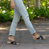 Pair of black leather Catalina slide sandals with crisscross straps worn by a person walking on a stone path.