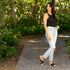 A woman wears black Catalina slide sandals with crossed straps on a stone path surrounded by green foliage.