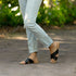 Pair of black leather Catalina Slide Sandals with crisscross straps worn with light-wash denim jeans on a stone path.