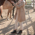 A person wearing black leather Eva Everyday Chelsea Boots, white pants, and a tan cardigan stands outdoors near a horse.