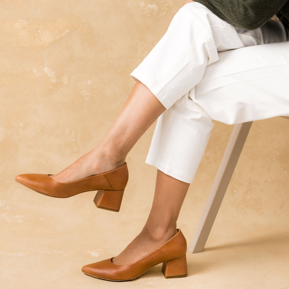 Pair of caramel leather pointed-toe pumps with a block mid heel worn with white trousers.